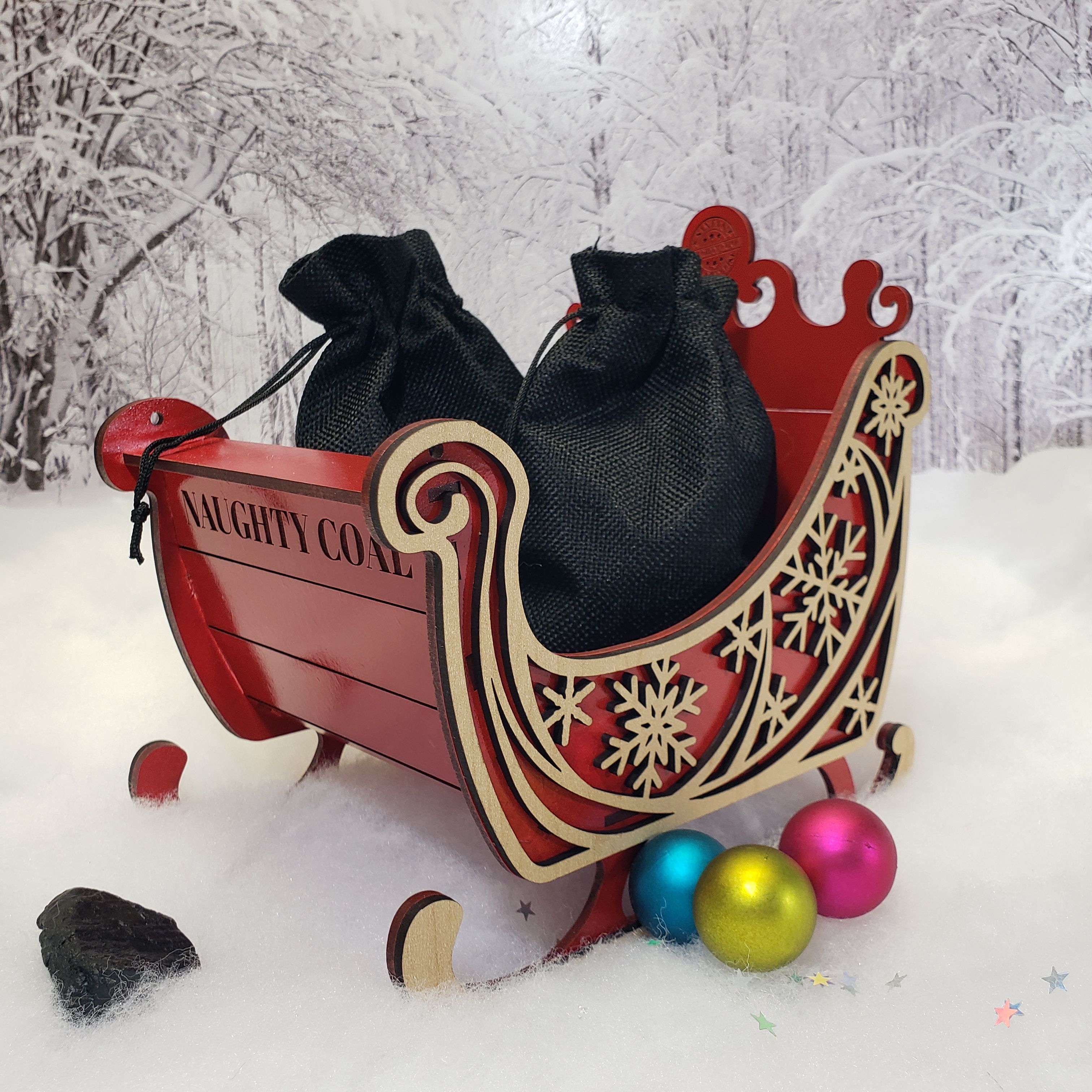 Red Naughty Coal sleigh with spilling sacks and holiday ornaments on white snow background – handmade gag gift.